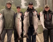 Four people stand on a dock, showcasing their salmon catch from a successful fishing trip on the Columbia River.