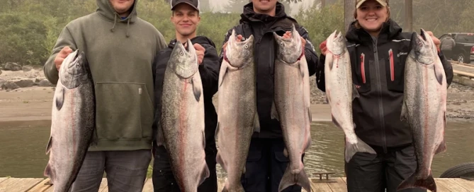 Four people stand on a dock, showcasing their salmon catch from a successful fishing trip on the Columbia River.