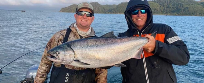 Two men on a boat showcasing a fish caught during their chinook fishing trip.