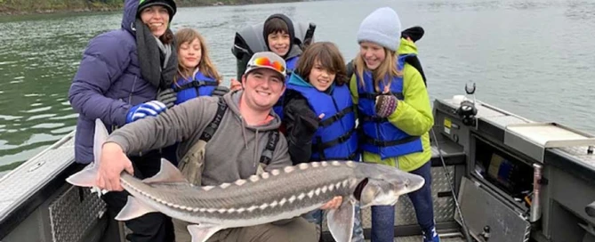 A group on a boat holding a large fish, enjoying sturgeon fishing on the Columbia River.