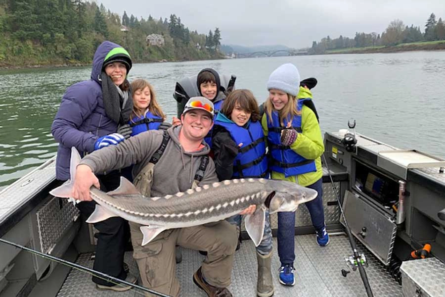 A group on a boat holding a large fish, enjoying sturgeon fishing on the Columbia River.
